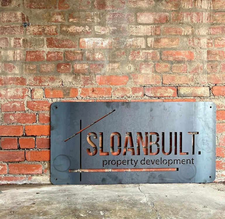 Metal Sloan Built sign against a brick wall.